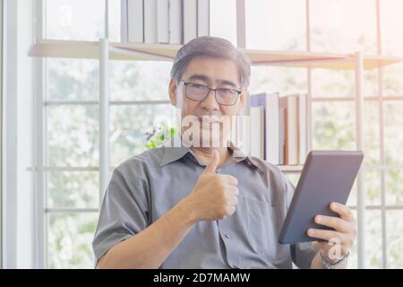 Un uomo asiatico di mezza età che usa un iPad in mano si sente fantastico. Foto Stock