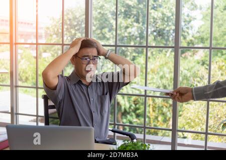 La mano che consegna documenti a un uomo asiatico di mezza età addolorante con la cattiva notizia: Imprenditori disperati vengono licenziati, nascosti, piangendo, delusi Foto Stock