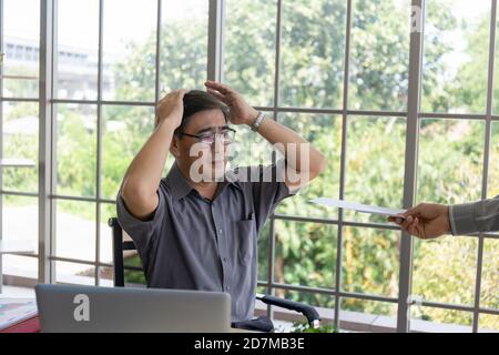 La mano che consegna documenti a un uomo asiatico di mezza età addolorante con la cattiva notizia: Imprenditori disperati vengono licenziati, nascosti, piangendo, delusi Foto Stock