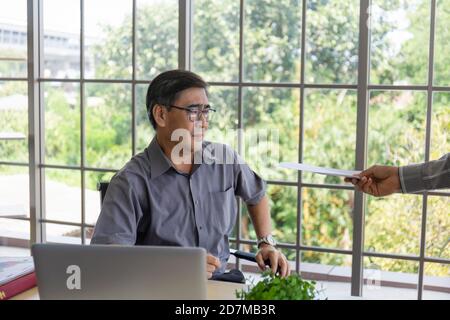 La mano che consegna documenti a un uomo asiatico di mezza età addolorante con la cattiva notizia: Imprenditori disperati vengono licenziati, nascosti, piangendo, delusi Foto Stock