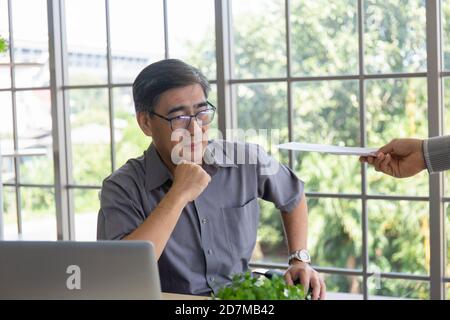 La mano che consegna documenti a un uomo asiatico di mezza età addolorante con la cattiva notizia: Imprenditori disperati vengono licenziati, nascosti, piangendo, delusi Foto Stock