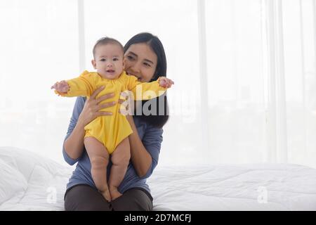 Una mamma asiatica sta giocando felicemente con il suo bambino a letto. Foto Stock