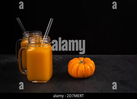 Due vaschette quadrate in vetro con coda di zucca non alcolica e cannucce in vetro su superficie nera. La zucca intera è vicino a vasetti. Backgroun orizzontale Foto Stock