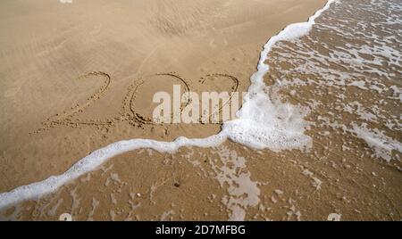 l'anno 2020 in tet scritto in sabbia sulla spiaggia è coperto da onde oceaniche e scompare Foto Stock
