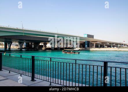 Barca tradizionale degli emirati conosciuta come Abra passando sotto il ponte nel canale d'acqua di Dubai. EMIRATI ARABI UNITI. All'aperto. Foto Stock