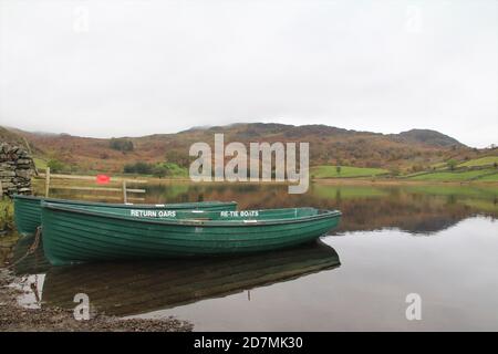 barche a remi ormeggiate su un tranquillo lago circondato da colline e alberi Foto Stock