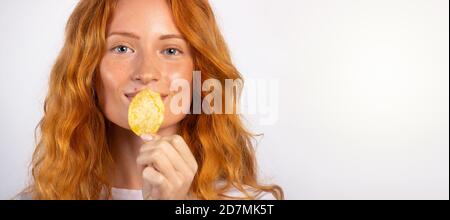 Giovane bella ragazza che mangia patatine su sfondo bianco con spazio vuoto laterale. Banner - formato lungo Foto Stock