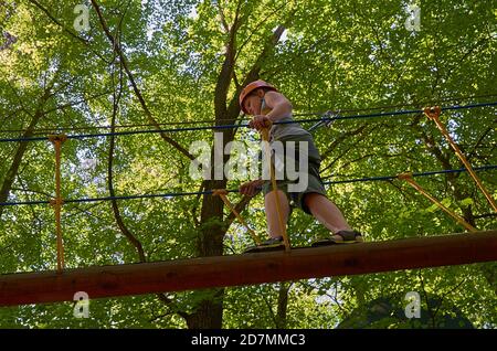 Un ragazzo con un casco e un'assicurazione passa un percorso ad ostacoli ad alta quota. Allenamento Foto Stock