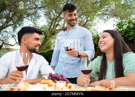 Tre simpaticissimi giovani festeggiano all'aperto con vino rosso Occhiali - eleganti amici millenari divertirsi in giardino bere alcoho Foto Stock