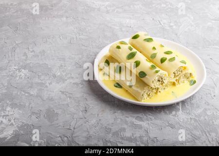 Cannelloni con salsa all'uovo, formaggio cremoso e foglie di origano su fondo grigio in cemento. Vista laterale, spazio copia. Foto Stock