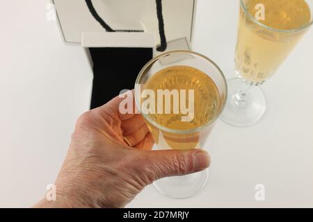 Mano della donna matura che tiene un bicchiere di champagne con ring box sfocato e un secondo bicchiere di champagne sullo sfondo. Foto Stock