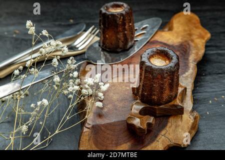 Cannelés (Canelés) de Bordeaux la ricetta è una piccola pasta con rum e vaniglia su un piatto di legno. Dolce tradizionale francese con gustosi spuntini. Obliquo Foto Stock