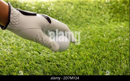 Palla da golf in mano con guanti, campo verde prato sfondo, vista ravvicinata. Golf sport e club concetto. Spazio di copia, modello Foto Stock