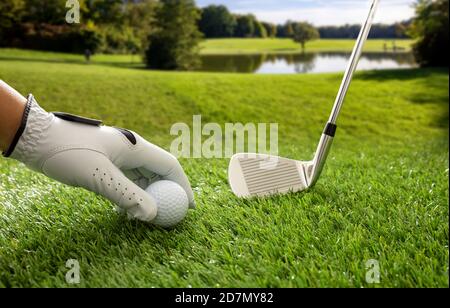Campo da golf, campo da golf e club su prato verde, sfondo blu cielo nuvoloso. Mano del golfer nel guanto che tiene una sfera, vista ravvicinata. Foto Stock
