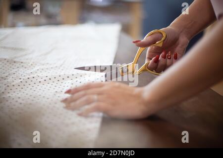 Mani donna ben curate che tagliano il tessuto a pois con il sarto forbici per abiti da cucire in studio Foto Stock
