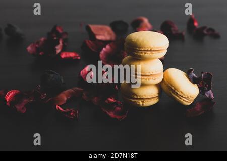 Primo piano della colazione con macaroni gialli al limone. Primo piano del dessert francese su sfondo nero e fiori intorno in un semplice vin Foto Stock