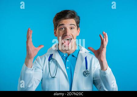 Il dottore stupito ha scioccato, dicendo WOW. Bel doc in cappotto medico sorpreso a macchina fotografica su sfondo blu. Foto Stock