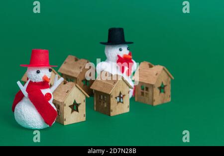 Closeup di due pupazzi di neve e piccole case di legno come Natale ornamenti su sfondo verde Foto Stock