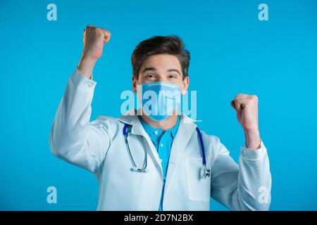 Sì gesto vincitore. Stupito medico in bianco cappotto professionale scioccato. Bell'uomo sorpreso a macchina fotografica su sfondo blu Foto Stock