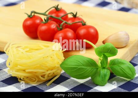 Pasta ingredienti: Tagliatelle non cotte, pomodori ciliegini su gambo e foglie di basilico fresco Foto Stock