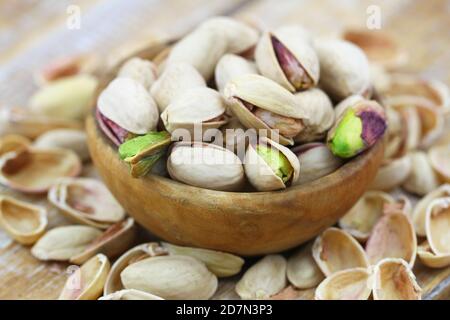 Pistacchio noci in ciotola di legno tra pistacchio aperto noci sopra superficie in legno Foto Stock