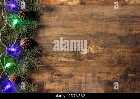 Rami di abete verde e luci di Natale su sfondo tavolo di legno scuro. Cornice creativa realizzata con rami di abete natalizio coni di pino su legno bac Foto Stock