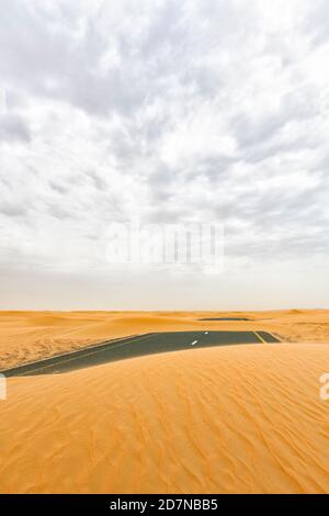 (Fuoco selettivo) vista mozzafiato di una strada deserta coperta da dune di sabbia che attraversano il deserto di Dubai. Dubai, Emirati Arabi Uniti, (UEA). Foto Stock