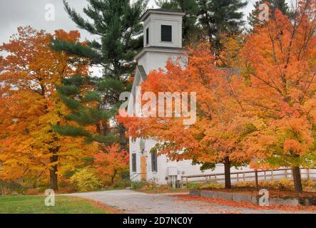 Autunno nella panoramica New England. Alberi di acero giallo e arancio brillanti che incorniciano la storica sala riunioni della città nel rurale Wilton Center, New Hampshire. Foto Stock