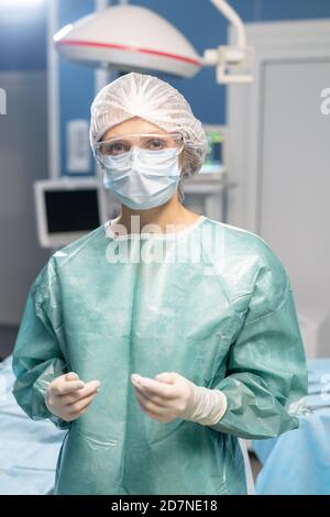 Giovane donna moderna chirurgo in guanti protettivi, maschera e occhiali Foto Stock