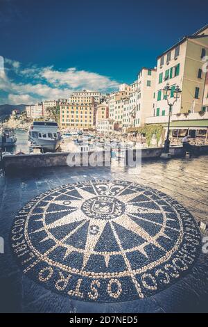 Bussola rosa. Mosaico di Windrose sulla strada a Camogli, città italiana. Porto e palazzi in cima. Rosa dei venti mosaico di pietra. Foto Stock