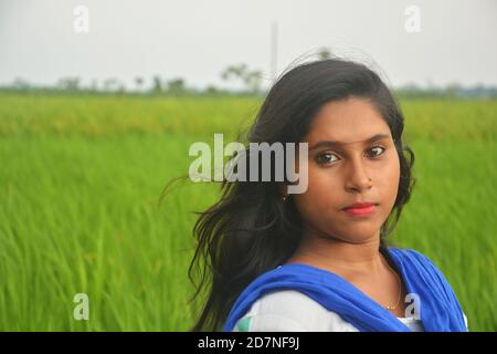 Primo piano di una ragazza adolescente che indossa salwar bianco e dhupatta blu con capelli lunghi in un campo di risaie verde, messa a fuoco selettiva Foto Stock