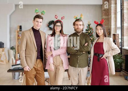 Fila di quattro giovani operai di colletti bianchi in casualwear intelligente e le fasce di natale Foto Stock