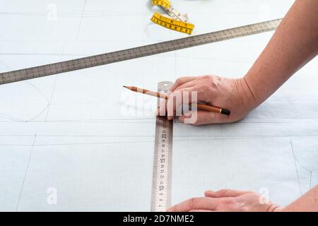 le mani del progettista con matita e righelli sul layout del pattern di abito disegnato su carta grafica a casa Foto Stock