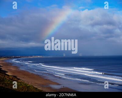 Vista sulla spiaggia di Saltburn che guarda verso Redcar al sole d'autunno cielo blu con un arcobaleno e una vista distante di Un Windfarm offshore Foto Stock