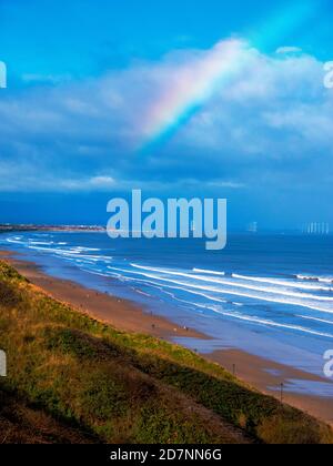 Vista sulla spiaggia di Saltburn che guarda verso Redcar al sole d'autunno cielo blu con un arcobaleno e una vista distante di Un Windfarm offshore Foto Stock