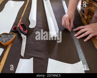 donna disegna modello di abito su tessuto marrone con regola da sapone a casa Foto Stock