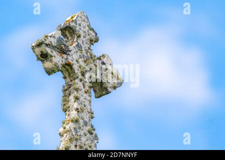 Looking up at a fancy white stone cross covered with moss and lichen. Partly cloudy blue shy above. Foto Stock