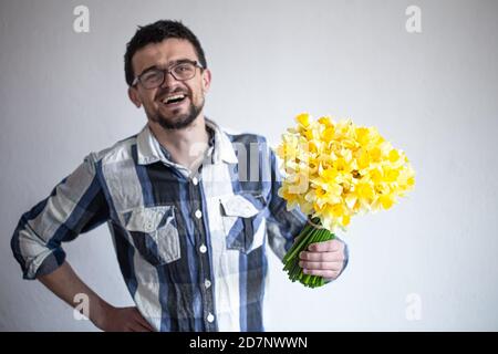 Un giovane in occhiali e una camicia con un bouquet di fiori. Su sfondo chiaro. Il concetto di saluto e di giorno della donna. Foto Stock