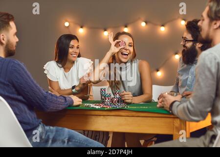 Felice giovane donna che copre il suo occhio con chip poker dopo vincere al casinò a tema festa con gli amici Foto Stock