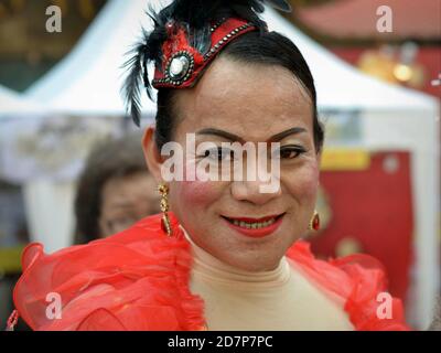 Medio invecchiato vestito thailandese cross-dressing genere queer (kathoey) sorride per la macchina fotografica a Chinatown durante il Capodanno cinese. Foto Stock