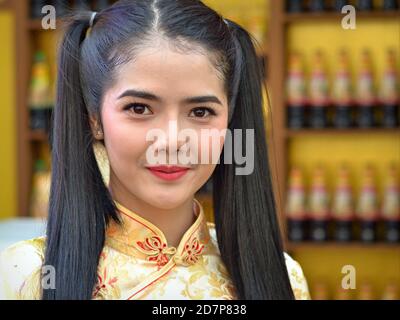 La giovane bellezza tailandese con i pigtail lunghi indossa un abito di seta tradizionale giallo e posa per la fotocamera nella Chinatown di Bangkok durante il capodanno cinese. Foto Stock