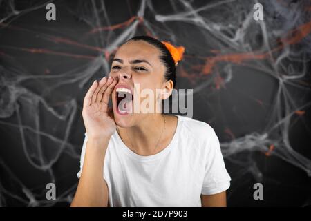 Giovane bella donna su sfondo nero con ciottoli e ragni gridare e gridare forte a fianco con la mano sulla bocca Foto Stock