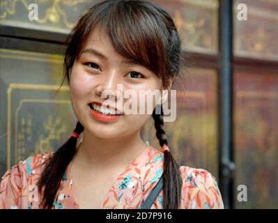 Giovane donna cinese tailandese con due trecce sorride per la telecamera nel Tempio del Drago Lotus di Bangkok (Wat Mangkon Kamala Wat) durante il capodanno cinese. Foto Stock