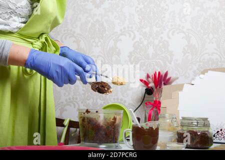 Una donna in guanti di gomma e una maschera macina datteri e burro di arachidi in un frullatore per fare caramelle. Cucinare caramelle da frutta secca e noci a casa in s. Foto Stock