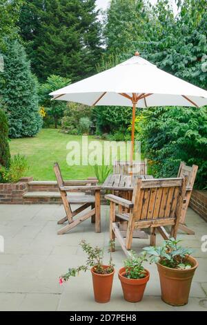 Giardino suburbano inglese in estate con patio, mobili da giardino in legno e un ombrellone o ombrellone Foto Stock