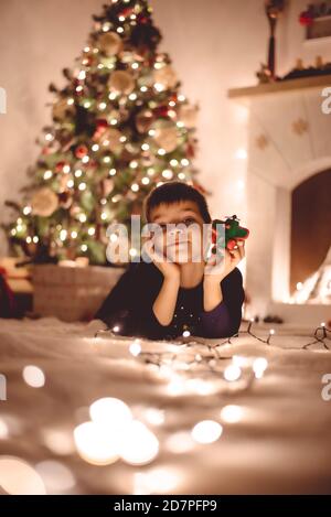 Il ragazzo carino sta giocando con l'aereo di santa sul pavimento Con molte luci alla vigilia di Natale Foto Stock