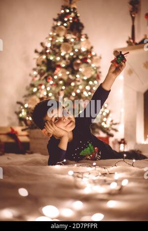 Il ragazzo carino sta giocando con l'aereo di santa sul pavimento Con molte luci alla vigilia di Natale Foto Stock