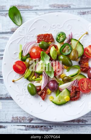 Insalata semplice con olive verdi e Kalamata, cetrioli, ciliegi e pomodori marinati, capperi e peperoni Jalapeno. Luminoso sfondo in legno. Foto Stock