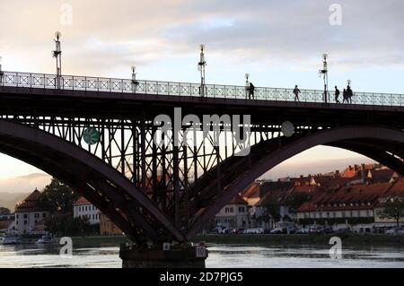 Persone che attraversano il Ponte Vecchio a Maribor al tramonto Foto Stock