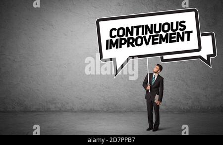 Giovane uomo d'affari in segno casuale di tenuta della strada con iscrizione CONTINUA DI MIGLIORAMENTO, nuovo concetto di idea di affari Foto Stock